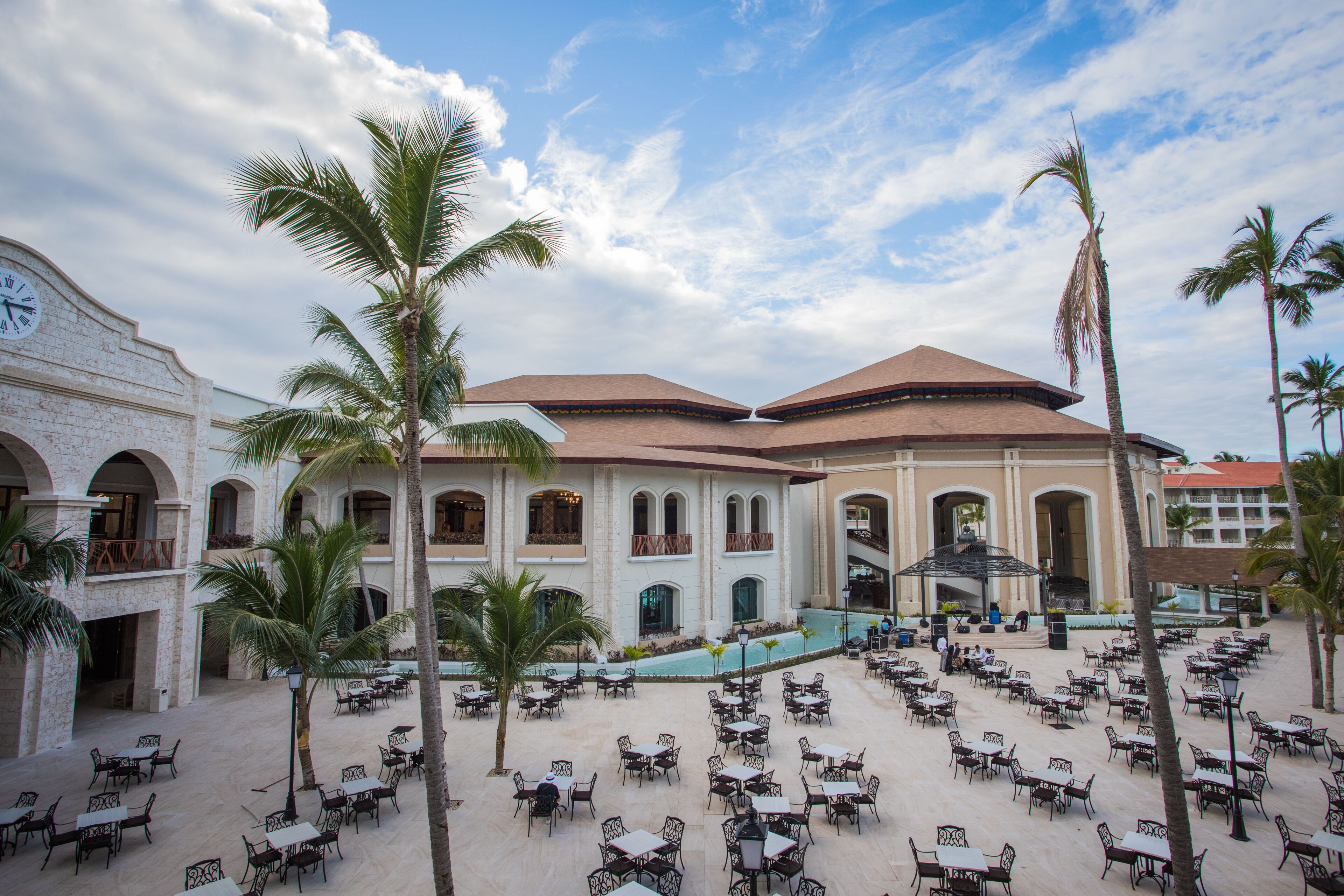 A courtyard with outdoor seating, palm trees, and a building with a clock.