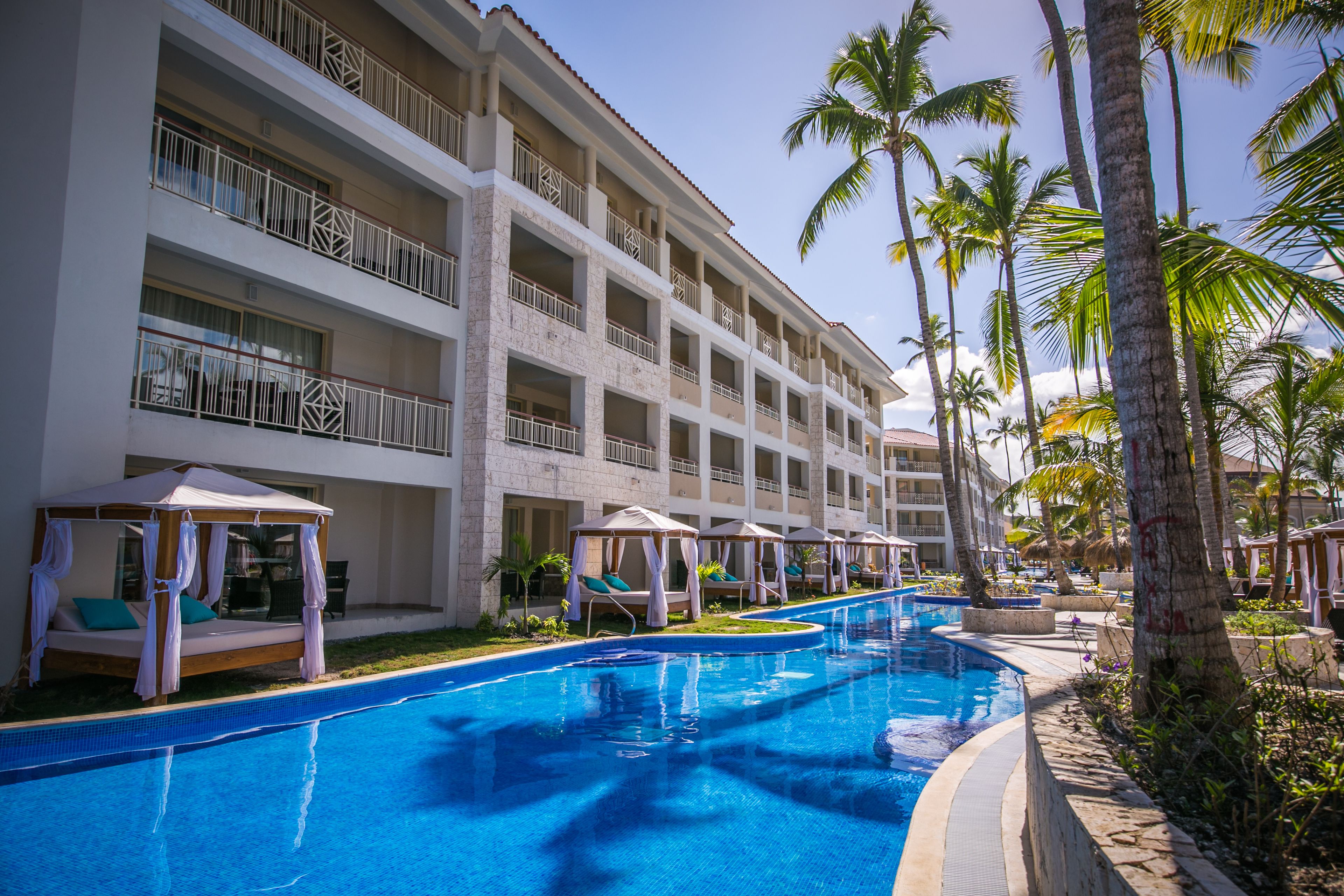 Un hotel con piscina, varios balcones y palmeras.