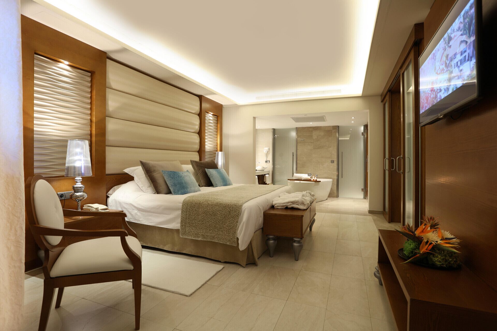 A modern hotel room with a large bed, bedside tables, a TV, and a bathroom with a bathtub.
