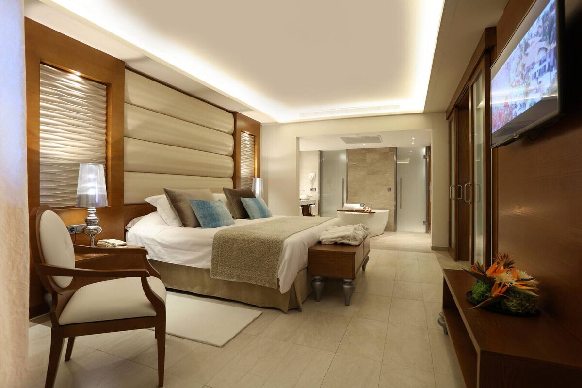 A modern hotel room with a large bed, bedside tables, a TV, and a bathroom with a bathtub.