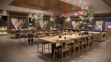 Un comedor moderno con varias mesas y sillas, detalles de madera y arreglos florales decorativos.