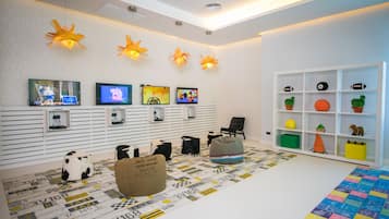 Una sala de estar moderna con piso blanco, una alfombra estampada, un sillón informal, una estantería y varias pantallas en la pared.