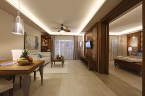 A hotel room with a dining area, a sofa, a television, and a bed.