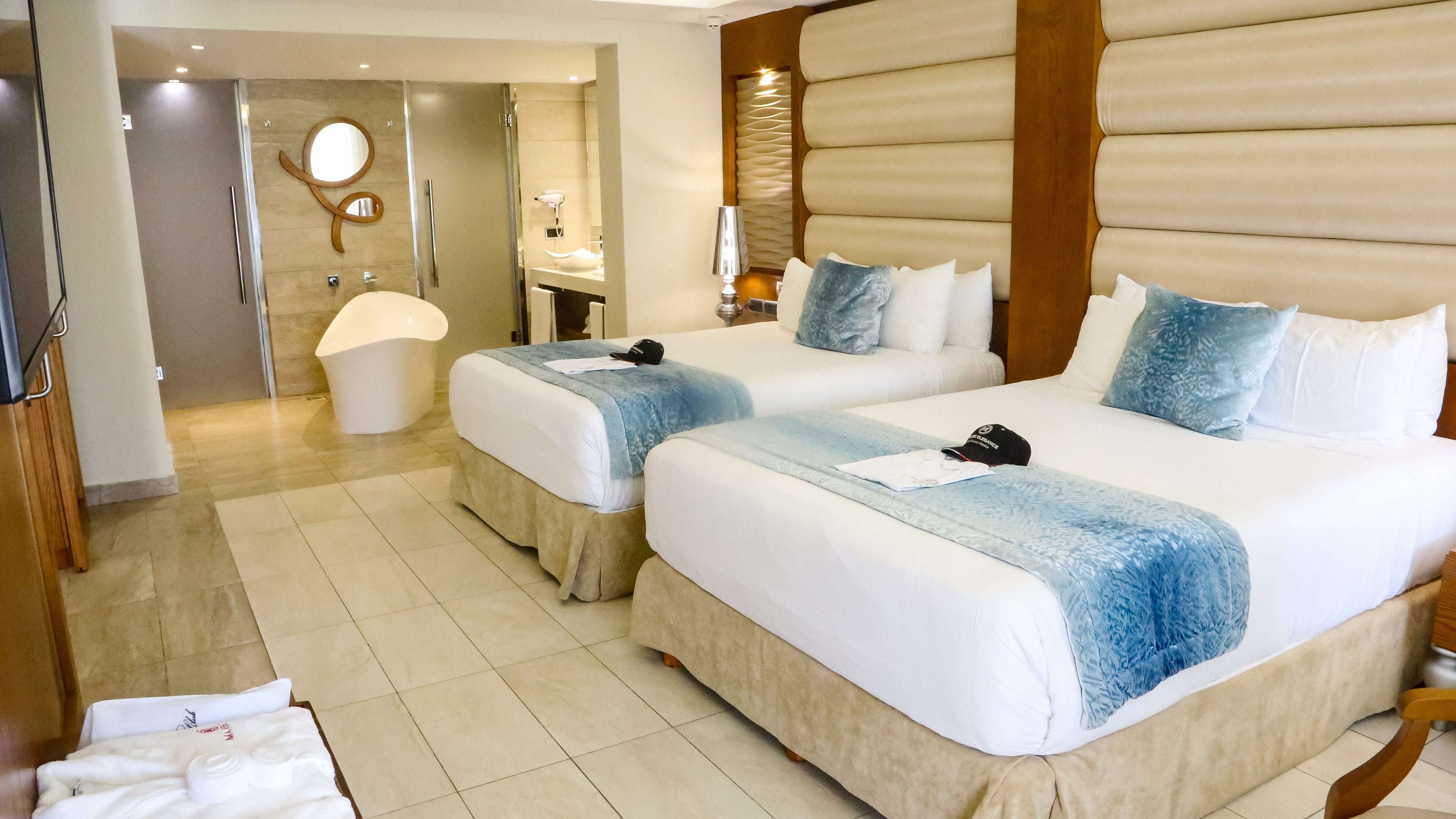 A hotel room with two beds, a bathroom, and a mirror.
