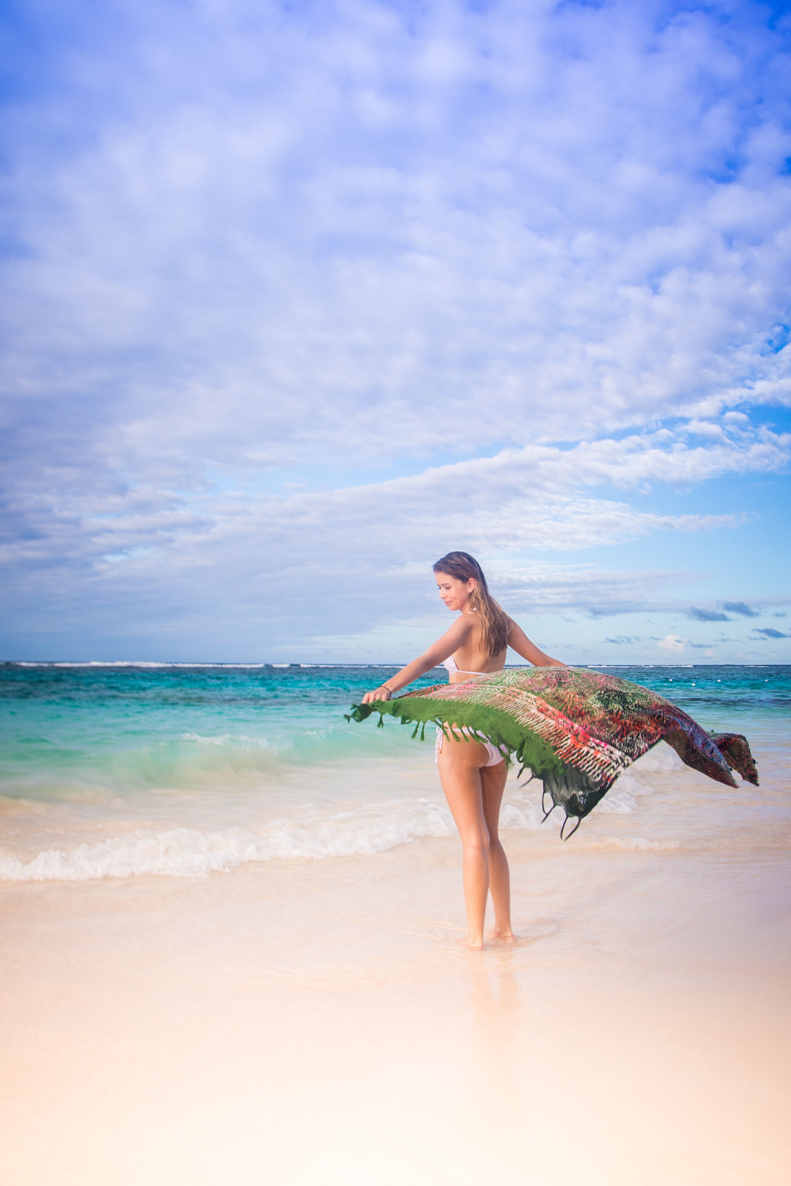 A person standing on a beach holding a colorful fabric.