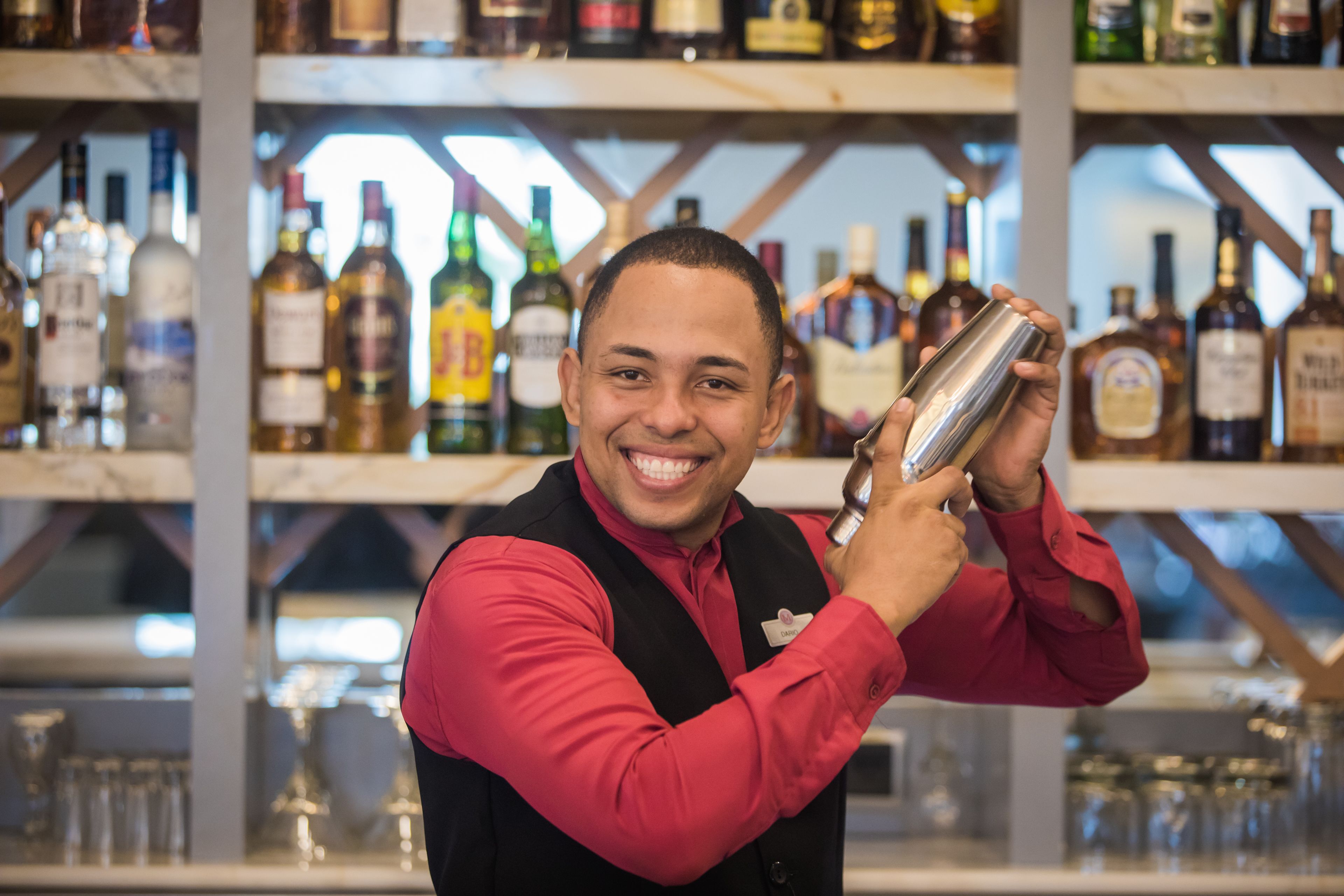 Un cantinero sosteniendo una coctelera en un bar con estantes llenos de botellas de licor al fondo.
