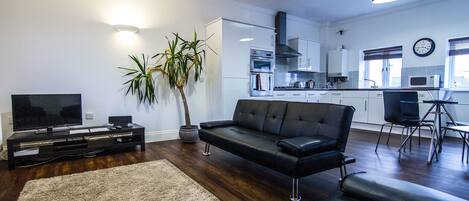 A modern living room with a black leather sofa, a flat-screen TV, and a potted plant.