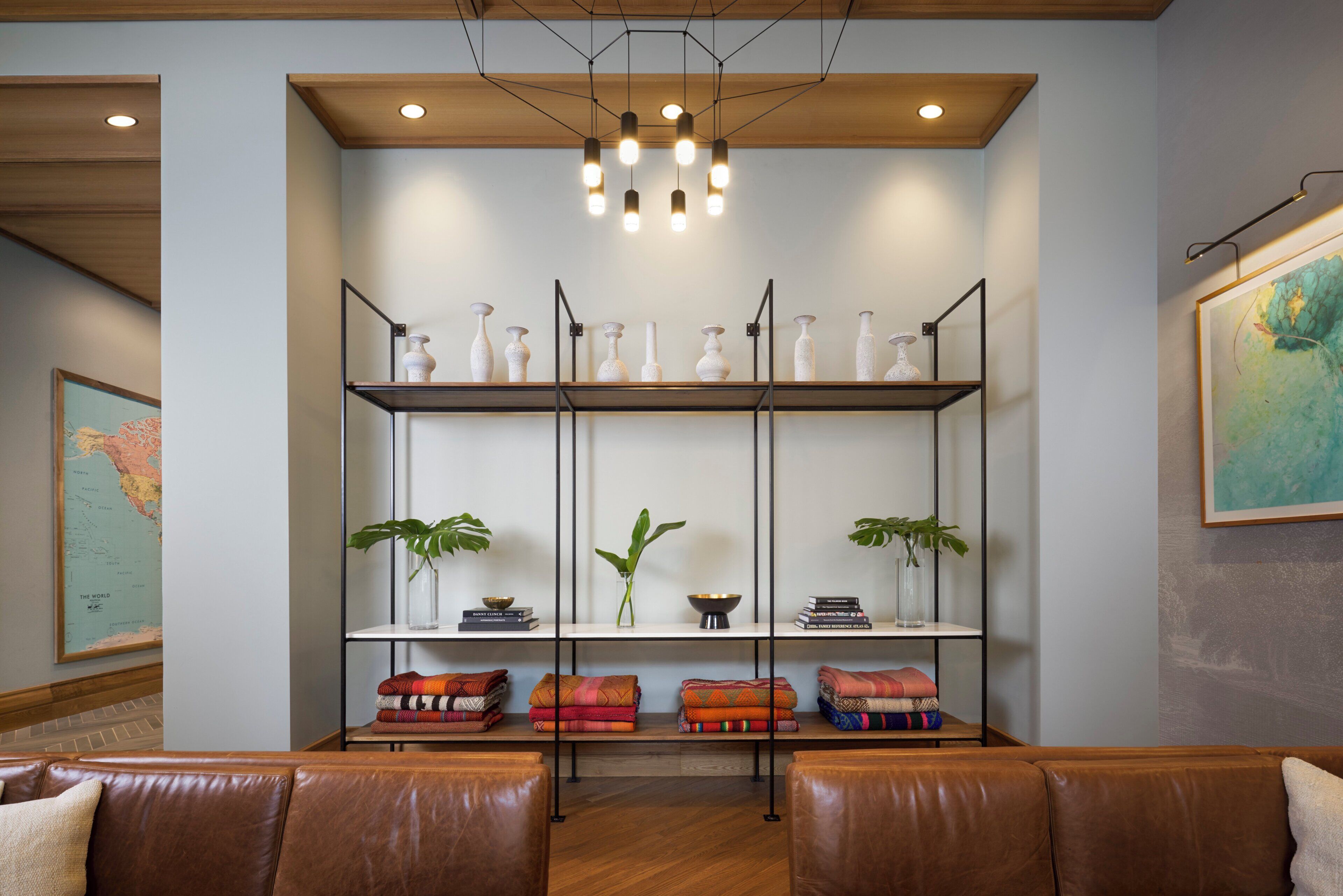 A room with a wooden ceiling, a hanging light fixture, a bookshelf with decorative vases, a globe map, and a couch with cushions.