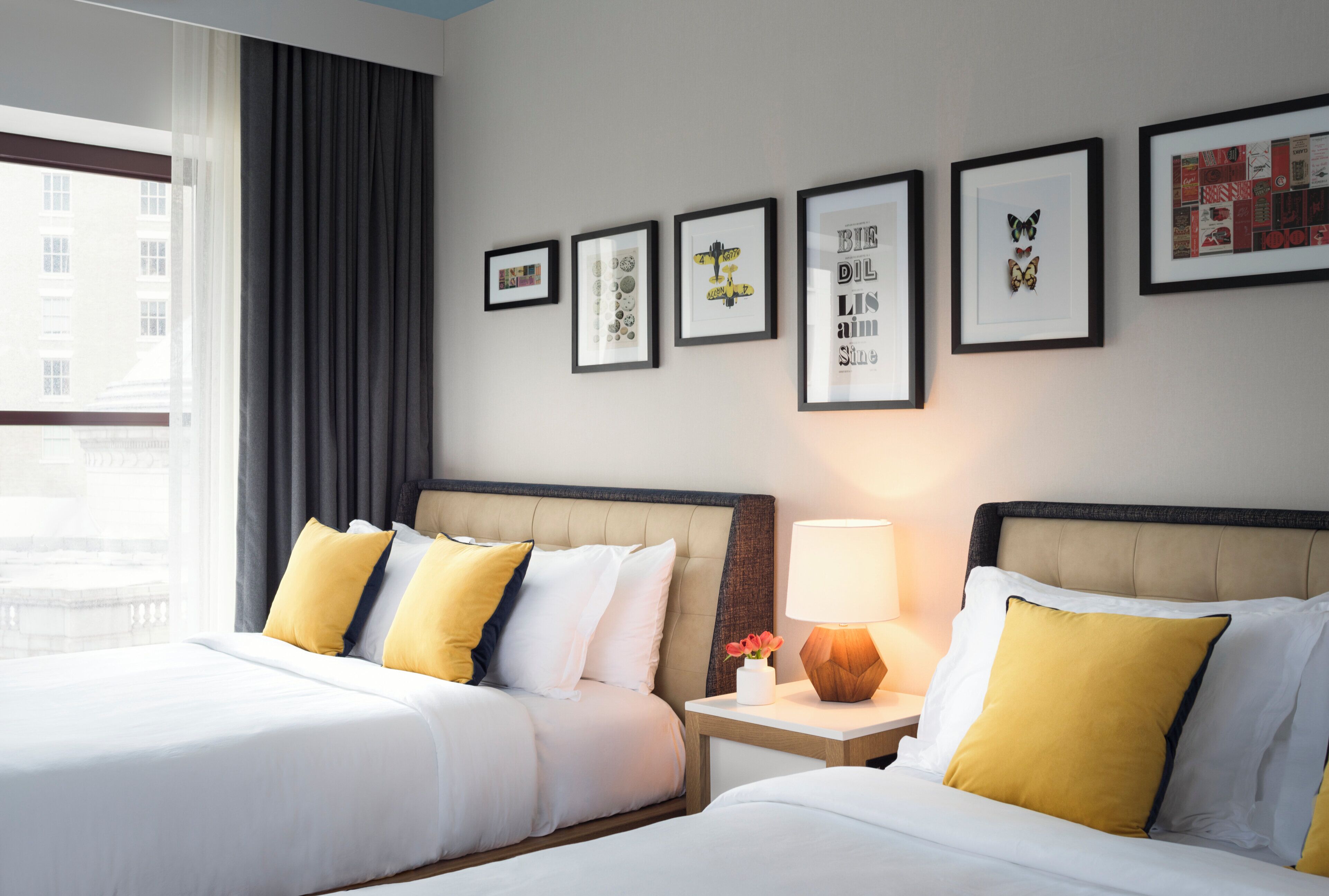 A hotel room with two beds, a nightstand with a lamp, and framed artwork on the wall.