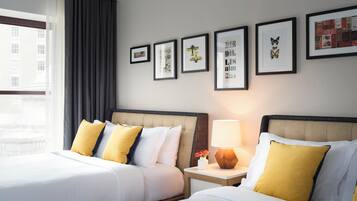 A hotel room with two beds, a nightstand with a lamp, and framed artwork on the wall.