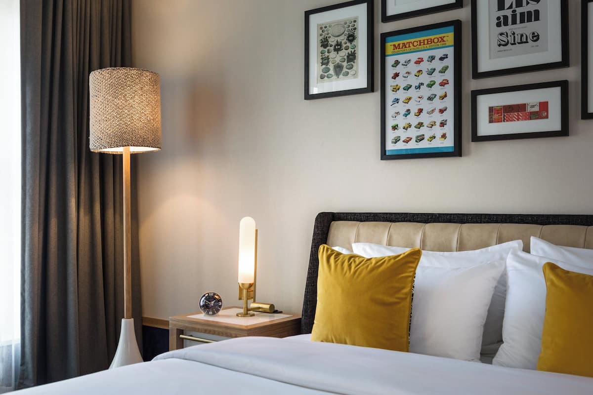 A hotel room with a bed, a nightstand, a lamp, and framed pictures on the wall.