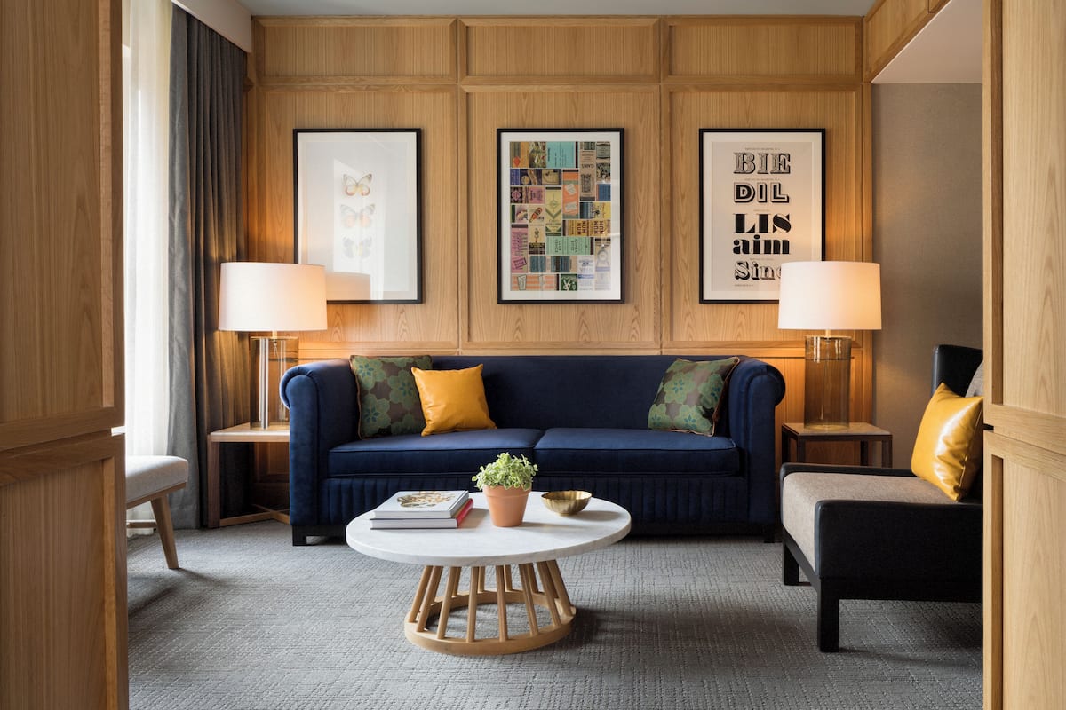 A modern living room with a dark blue sofa, two side tables with lamps, a round coffee table, and framed artwork on the wall.