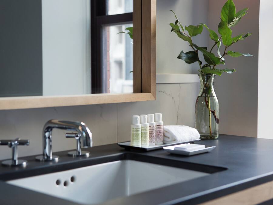 A bathroom with a mirror, sink, and a vase with a plant.