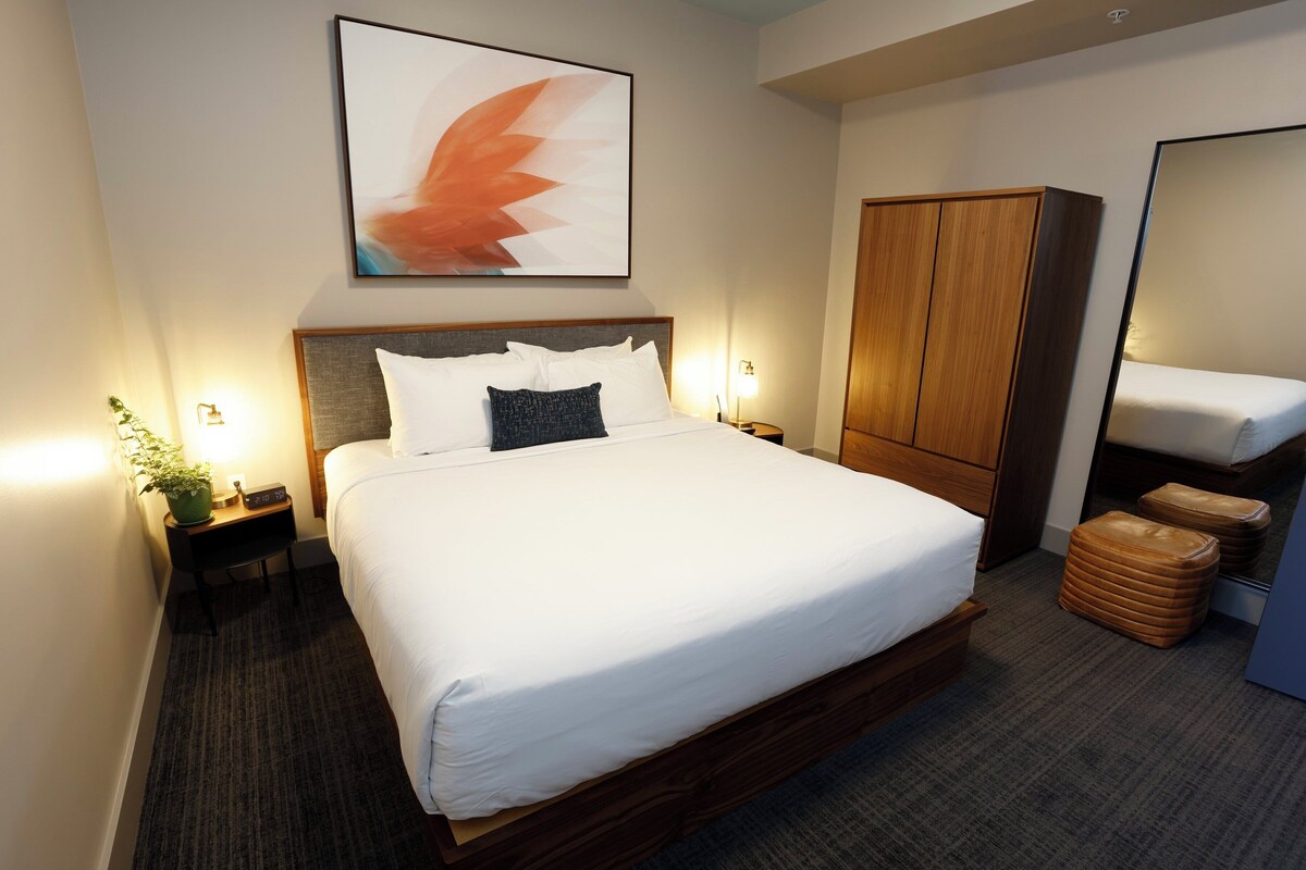 Een keurig ingerichte hotelkamer met een groot bed, een kledingkast, een nachtkastje met lamp en een kamerplant.