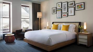 Quarto de hotel com uma cama grande, uma mesa de cabeceira, uma cadeira, um abajur e um painel com quadros.