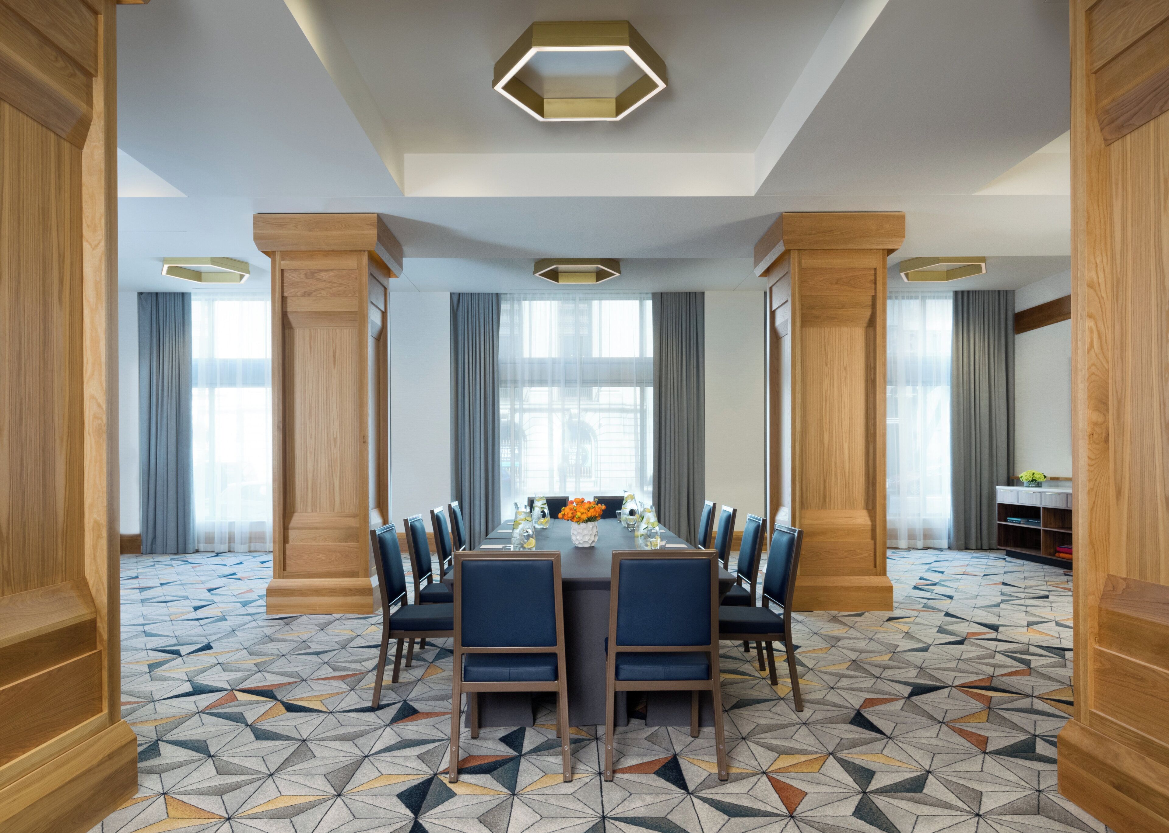 A conference room with a long table, blue chairs, and geometric patterned carpet.