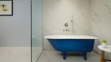 A modern bathroom with a blue clawfoot bathtub, a glass shower enclosure, and a marble wall.