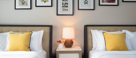 A hotel room with two beds, a nightstand with a lamp, and a wall decorated with framed pictures.