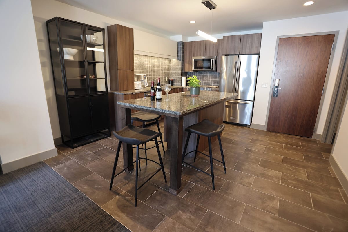 A modern kitchen with a central island, bar stools, stainless steel appliances, and a dark wood cabinet.