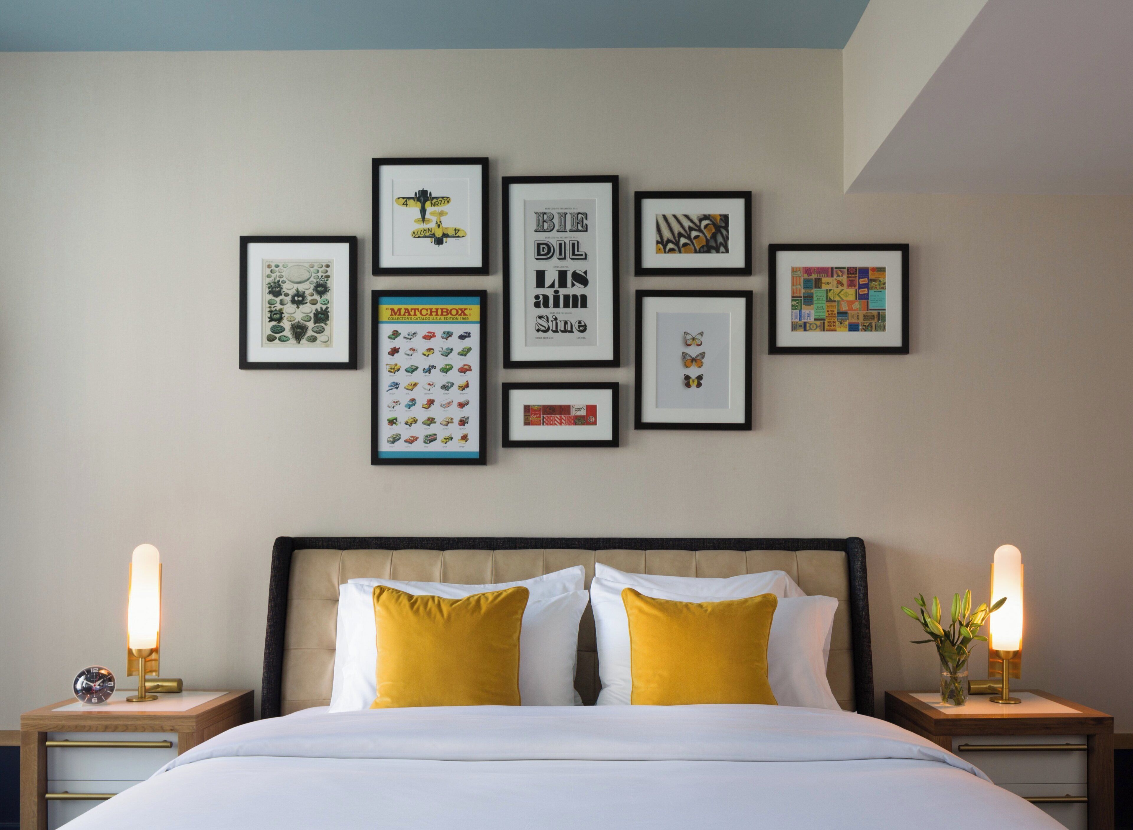 A neatly arranged bedroom with a bed, two bedside tables with lamps, and a wall adorned with various framed artworks.
