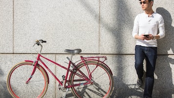 A person standing next to a red bicycle with a chain and gears, leaning against a textured wall.