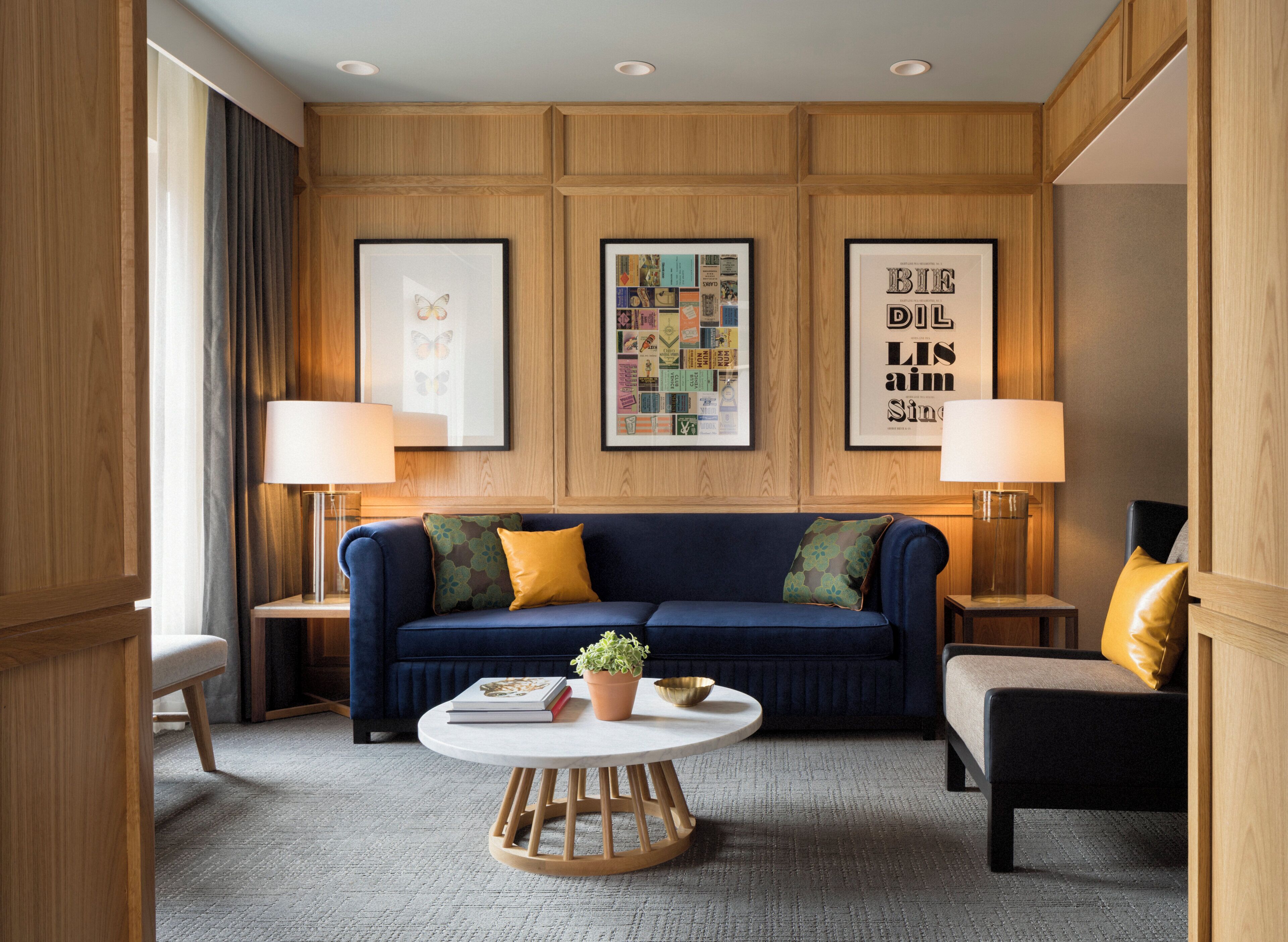 A modern living room with a blue sofa, two side tables with lamps, a round coffee table, and framed artwork on the walls.