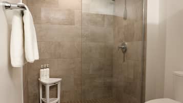 Et bruseområde med glasdør, et hvidt toilet og en lille hvid skammel med toiletartikler.