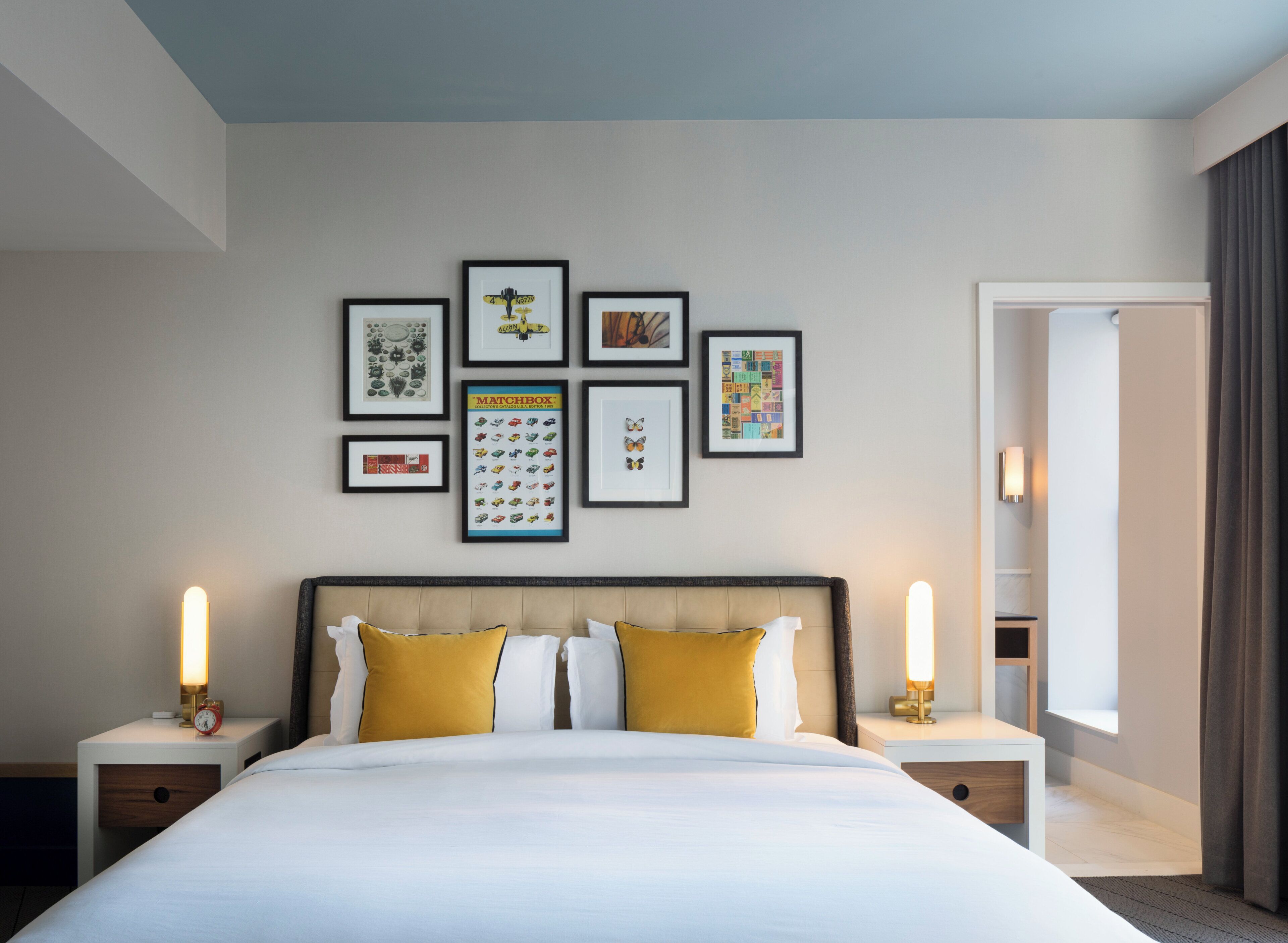A hotel room with a large bed, two bedside tables, a wall with framed artwork, and a window with curtains.