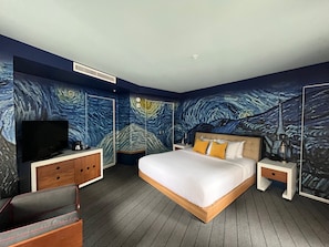 A modern hotel room with a large bed, a flat-screen TV, wooden furniture, and a wall mural.