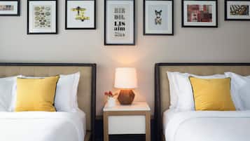 A hotel room with two beds, a nightstand with a lamp, and a wall with framed pictures.