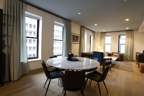 A modern hotel room with a round dining table, chairs, a sofa, and a small coffee table.