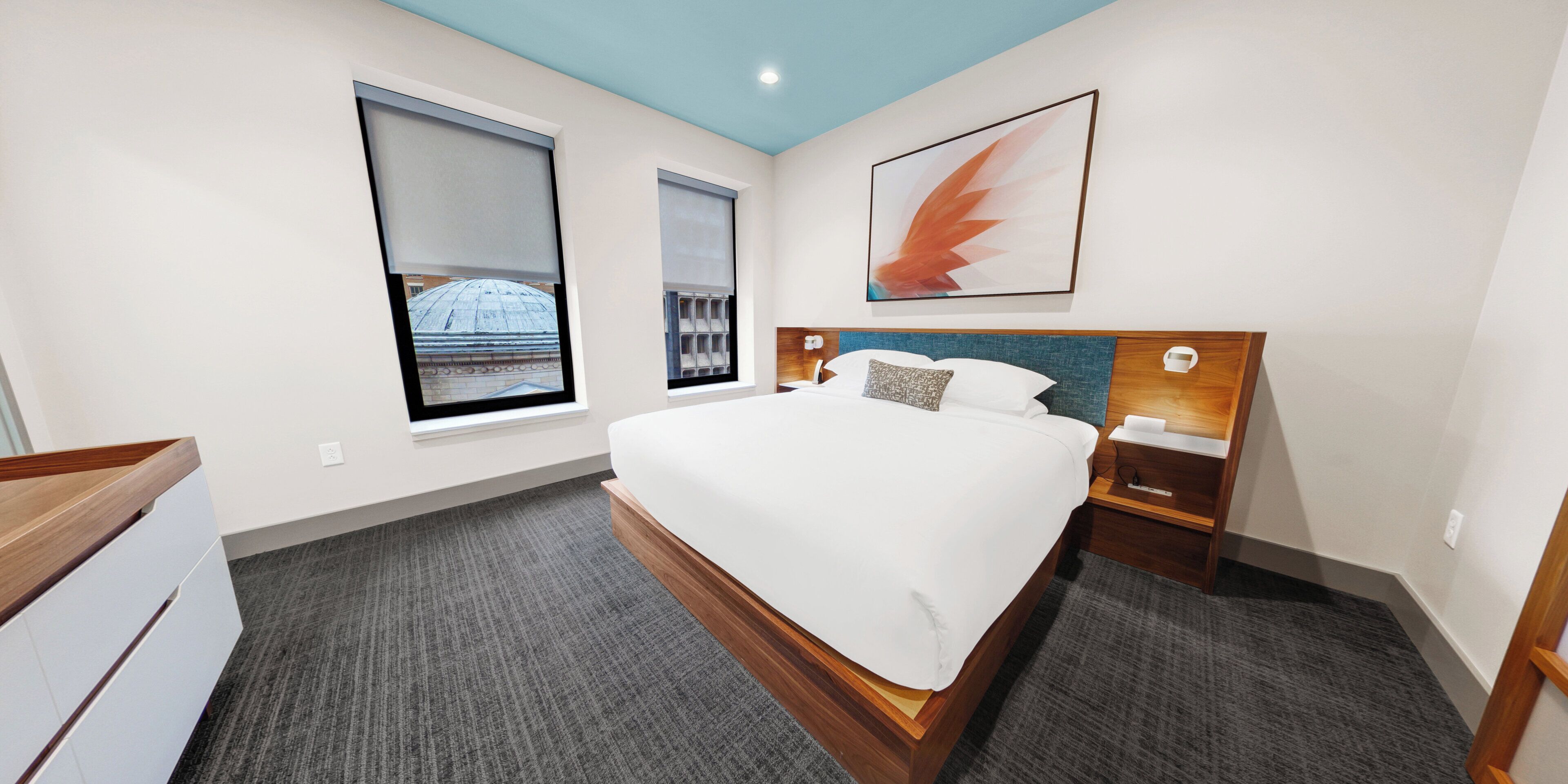 A modern hotel room with a large bed, a wooden headboard, a nightstand, and a window with a view of a dome structure.