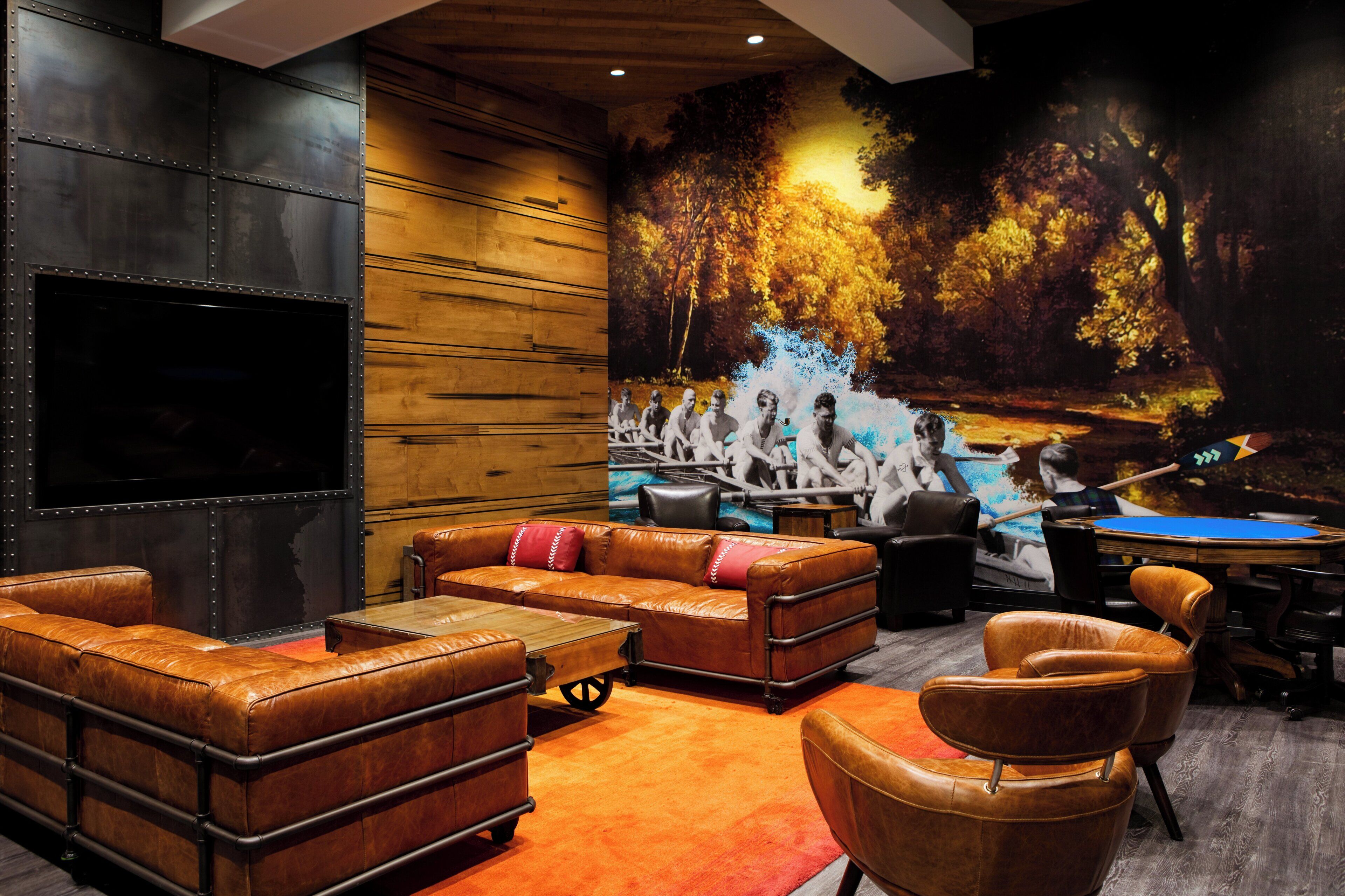 A modern lounge with leather sofas, a billiards table, and a large mural of a forest scene.