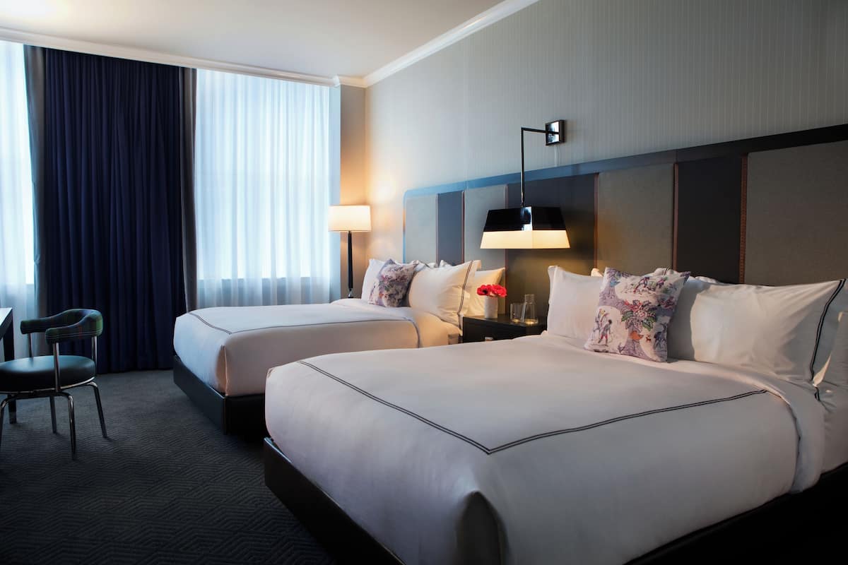 Ein Hotelzimmer mit zwei Betten, einem Schreibtisch, einem Sessel und einem großen Fenster mit Vorhängen.