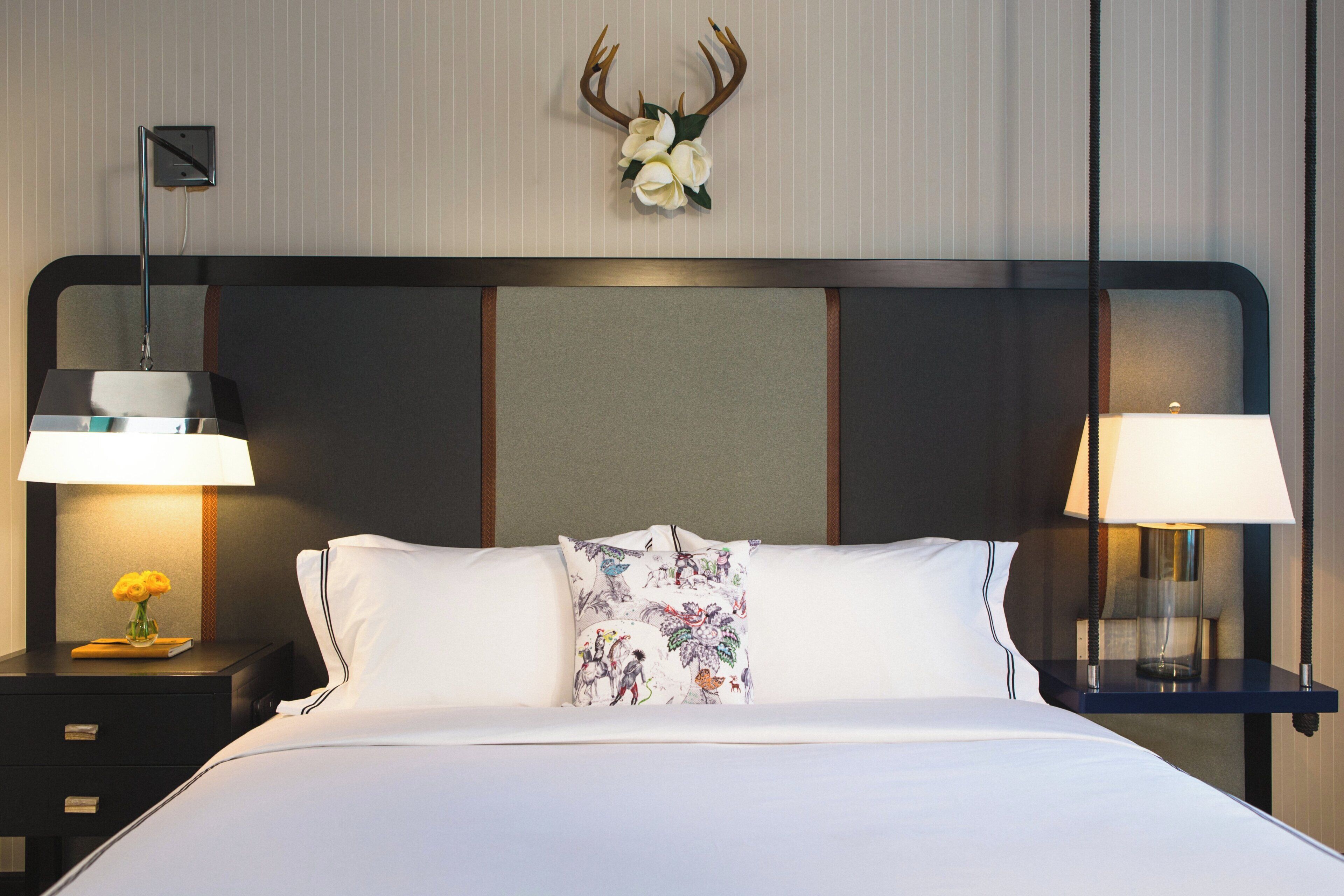 Habitació d'hotel amb un llit gran, dues taules de nit amb làmpades, una obra decorativa a la paret i un coixí amb motius florals.