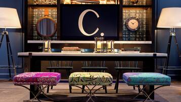 A bar area with a large illuminated letter C, bar stools, and a selection of books and bottles.