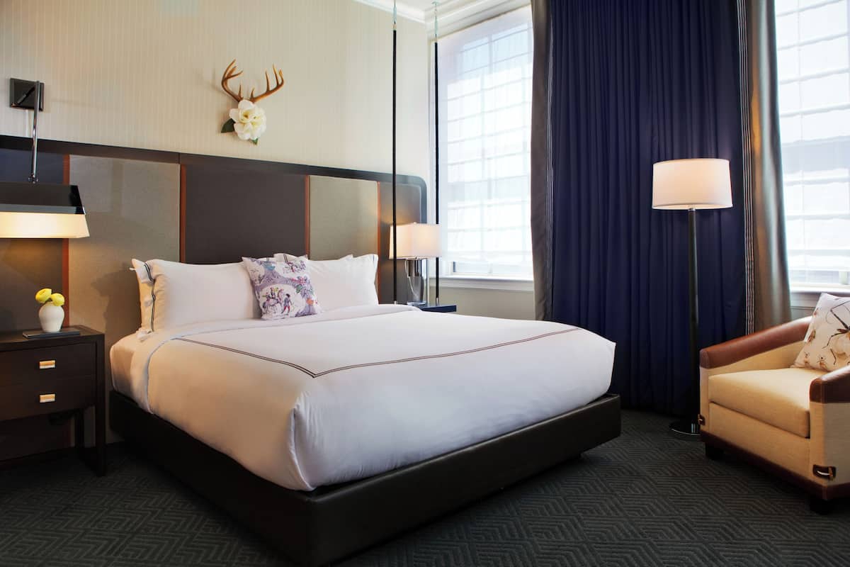 Ein Hotelzimmer mit einem großen Bett, zwei Nachttischen, einem Sessel, einer Wanddekoration mit einem Hirschgeweih und einem Fenster mit Vorhängen.