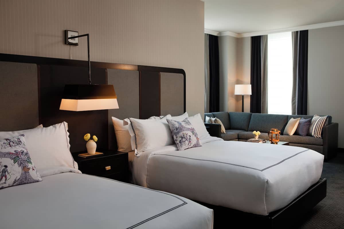 Ein Hotelzimmer mit zwei Betten, einem Schlafsofa, einem Nachttisch mit Lampe und Blick aus dem Fenster.