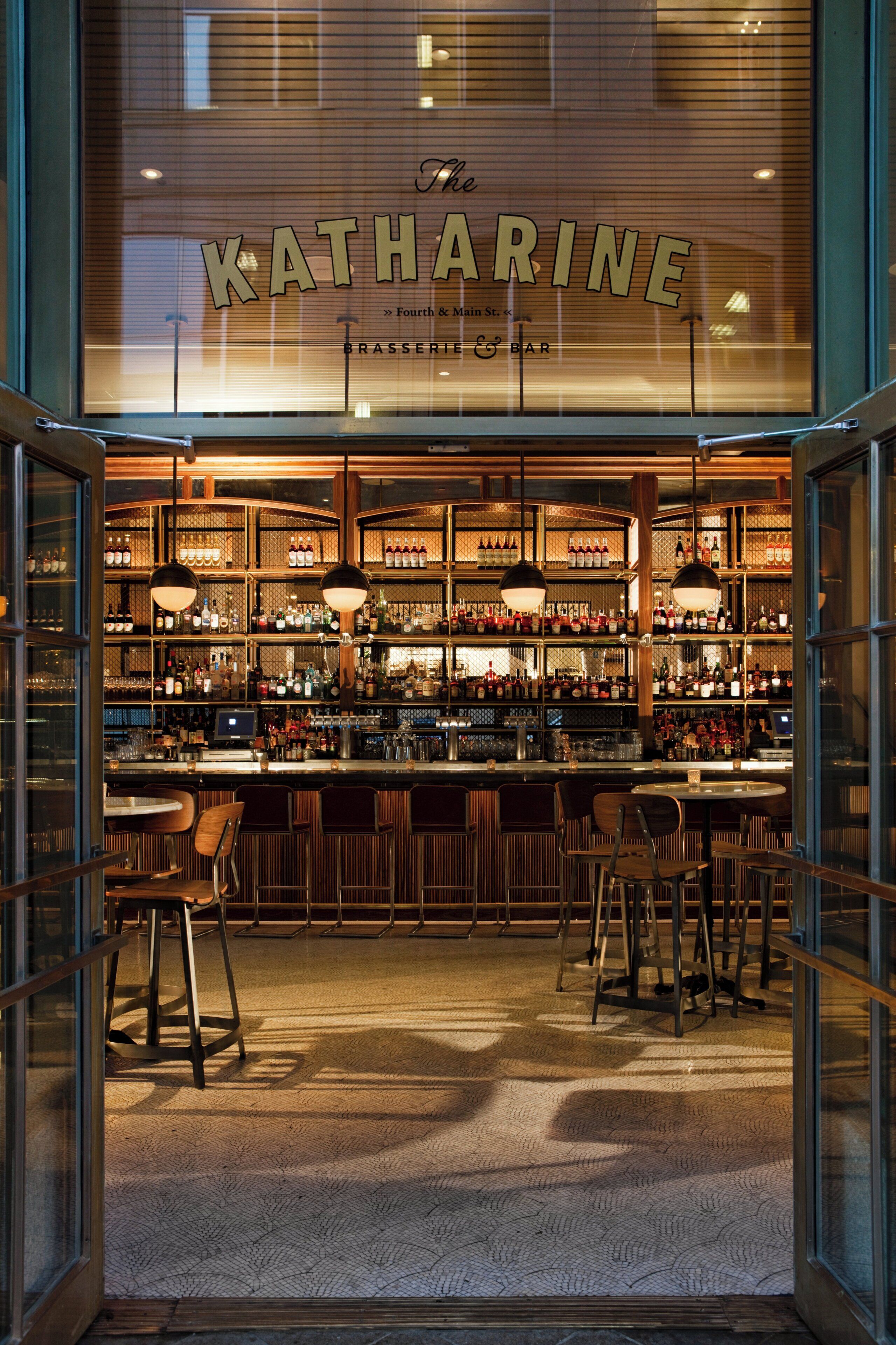 Un bar con fachada de vidrio, estantes llenos de botellas y taburetes.