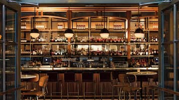 Un bar con fachada de vidrio, estantes llenos de botellas y taburetes.