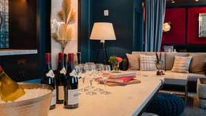 Un salon moderne avec une table basse en marbre, des bouteilles de vin, des verres et un canapé agrémenté de coussins décoratifs.