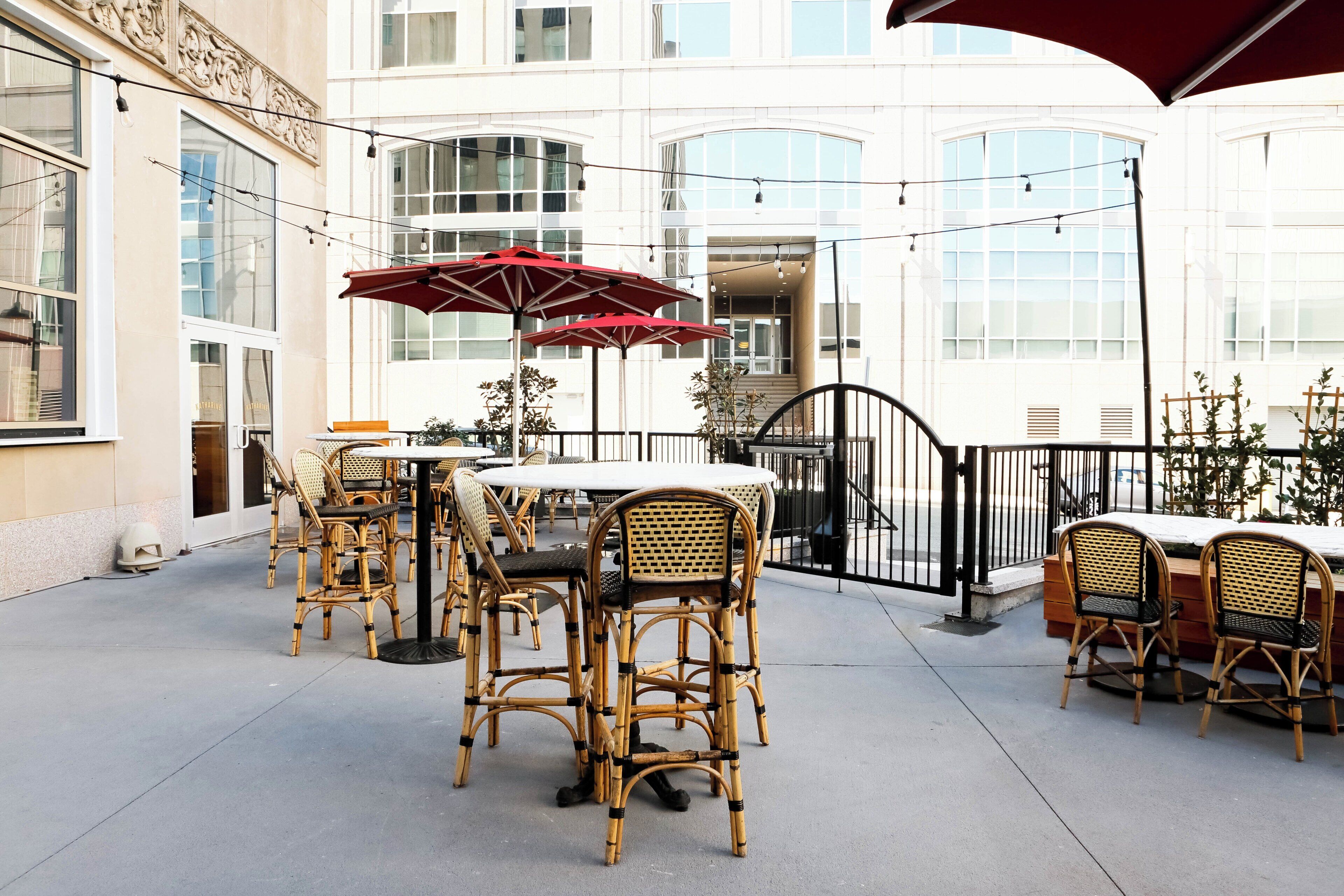 An outdoor patio area with wicker furniture, red umbrellas, and string lights.