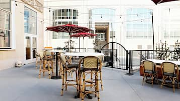 An outdoor patio area with wicker furniture, red umbrellas, and string lights.