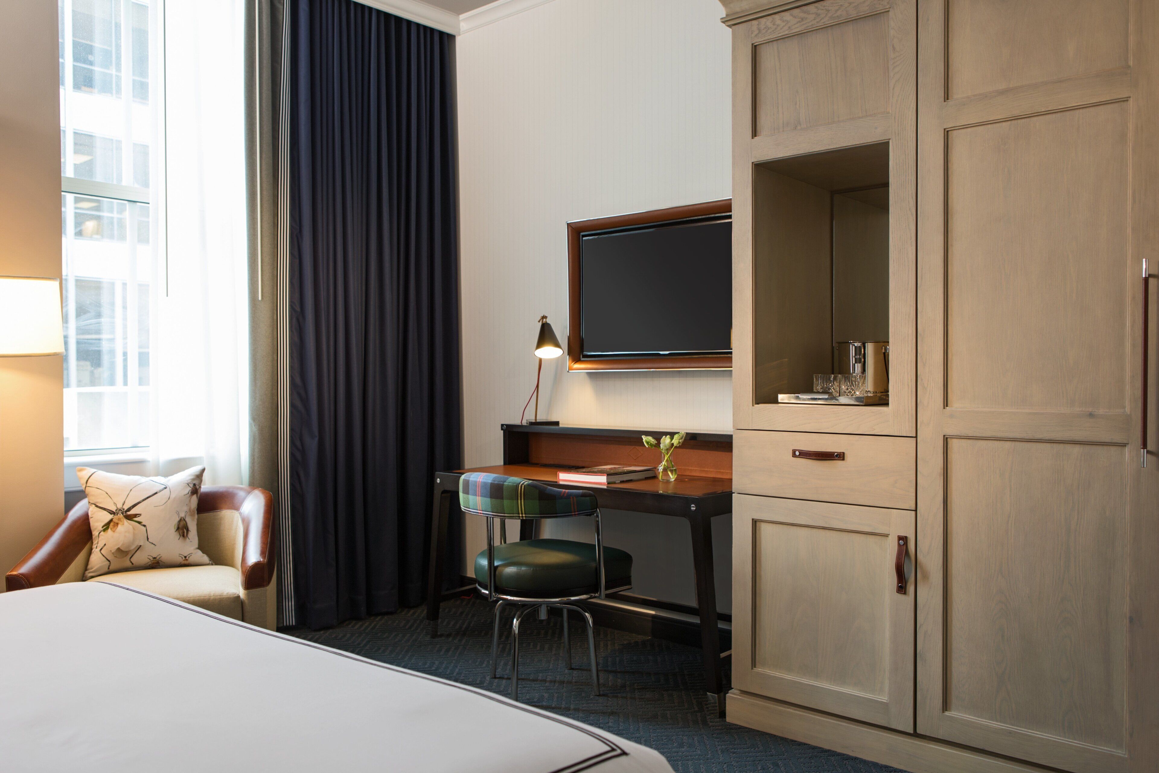 A hotel room with a bed, a desk with a chair, a television, and a wardrobe.