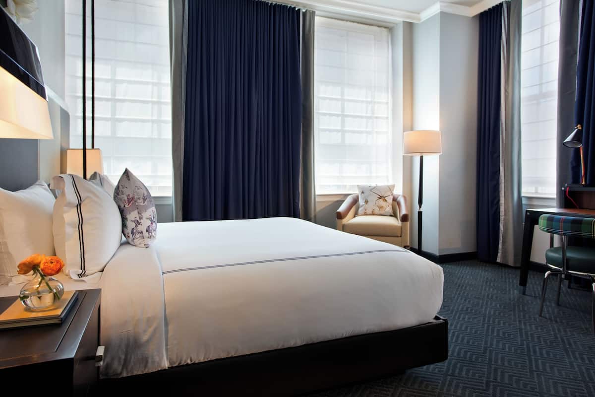 Ein Hotelzimmer mit einem großen Bett, einem Schreibtisch mit Lampe, einem Sessel und einem kleinen Tisch ebenfalls mit Lampe.