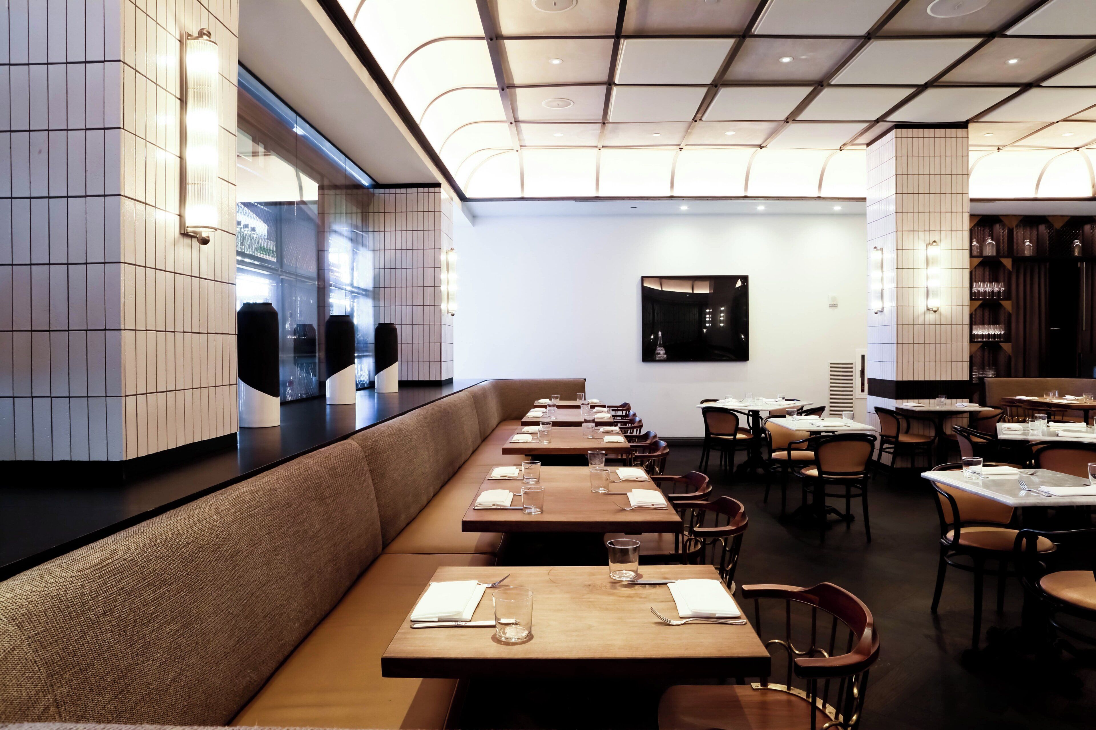L’intérieur d’un restaurant présente de longues tables en bois, des bancs rembourrés et un design moderne au niveau du plafond.