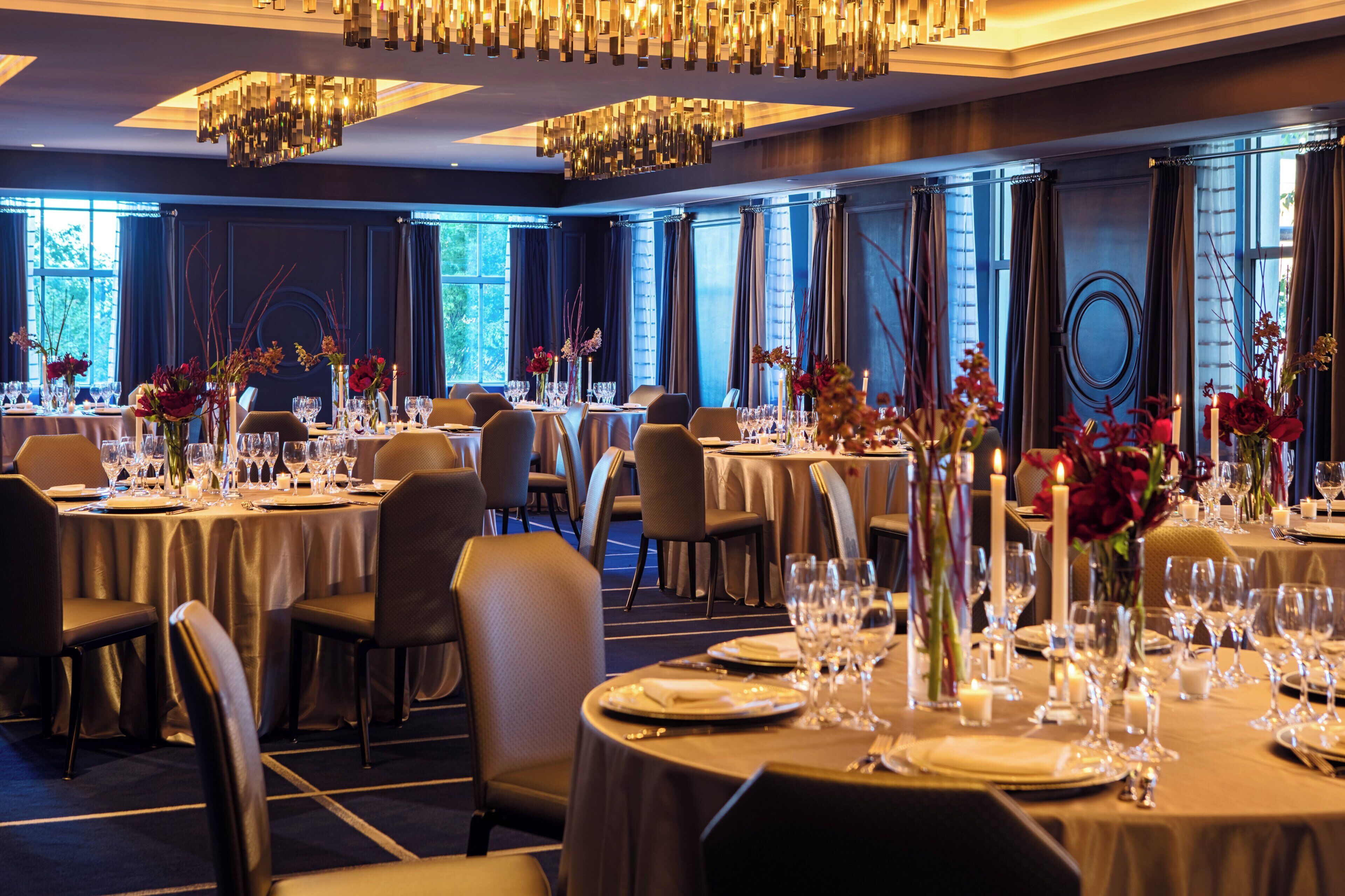 Un comedor formal con mesas redondas, sillas y centros de mesa con velas.