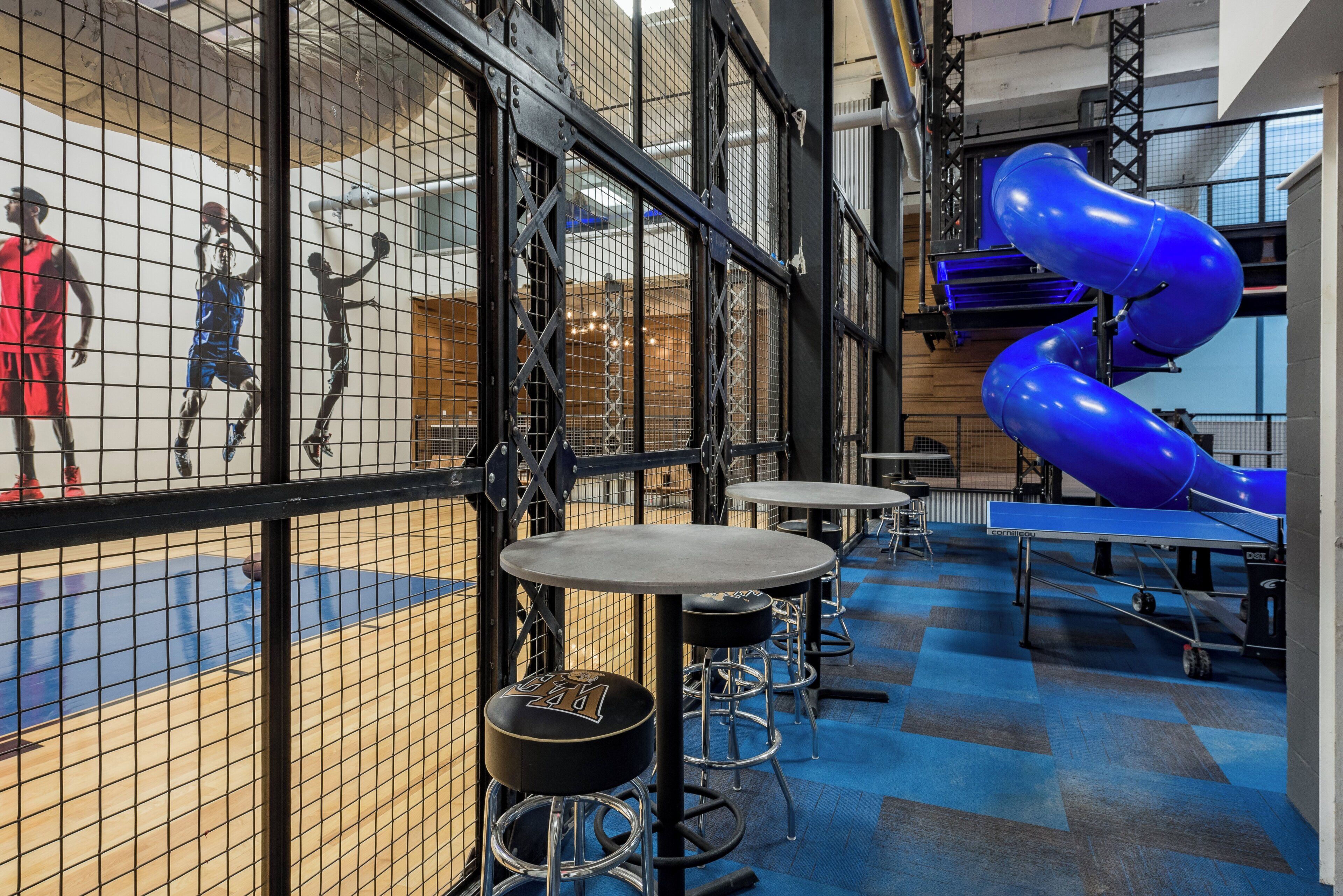 A sports facility with a basketball court, seating areas, and a blue slide.