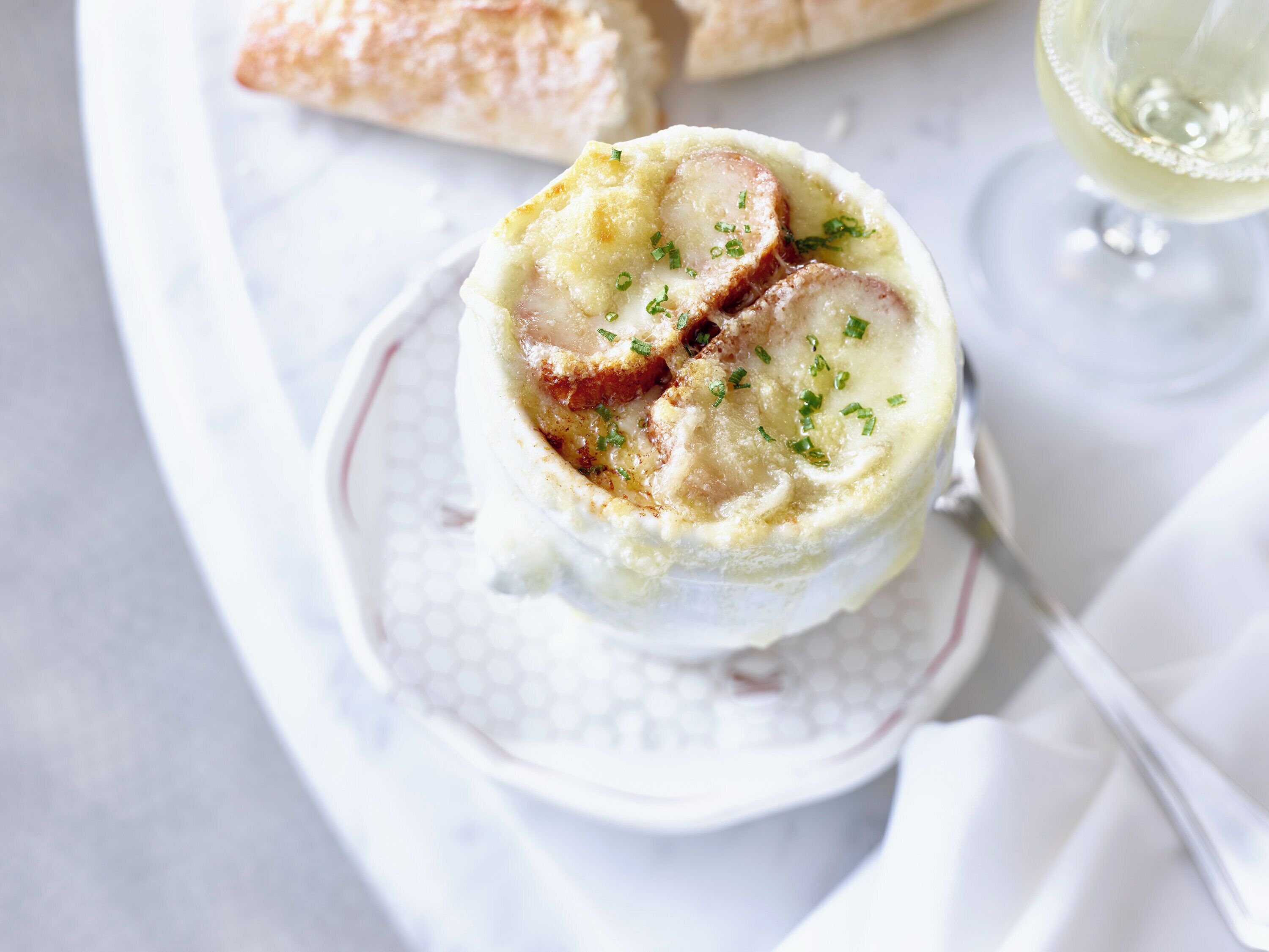 Un plat composé d’une sauce crémeuse et de tranches de viande, garni d’herbes, servi dans une assiette blanche avec une cuillère.