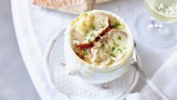 Un plat composé d’une sauce crémeuse et de tranches de viande, garni d’herbes, servi dans une assiette blanche avec une cuillère.